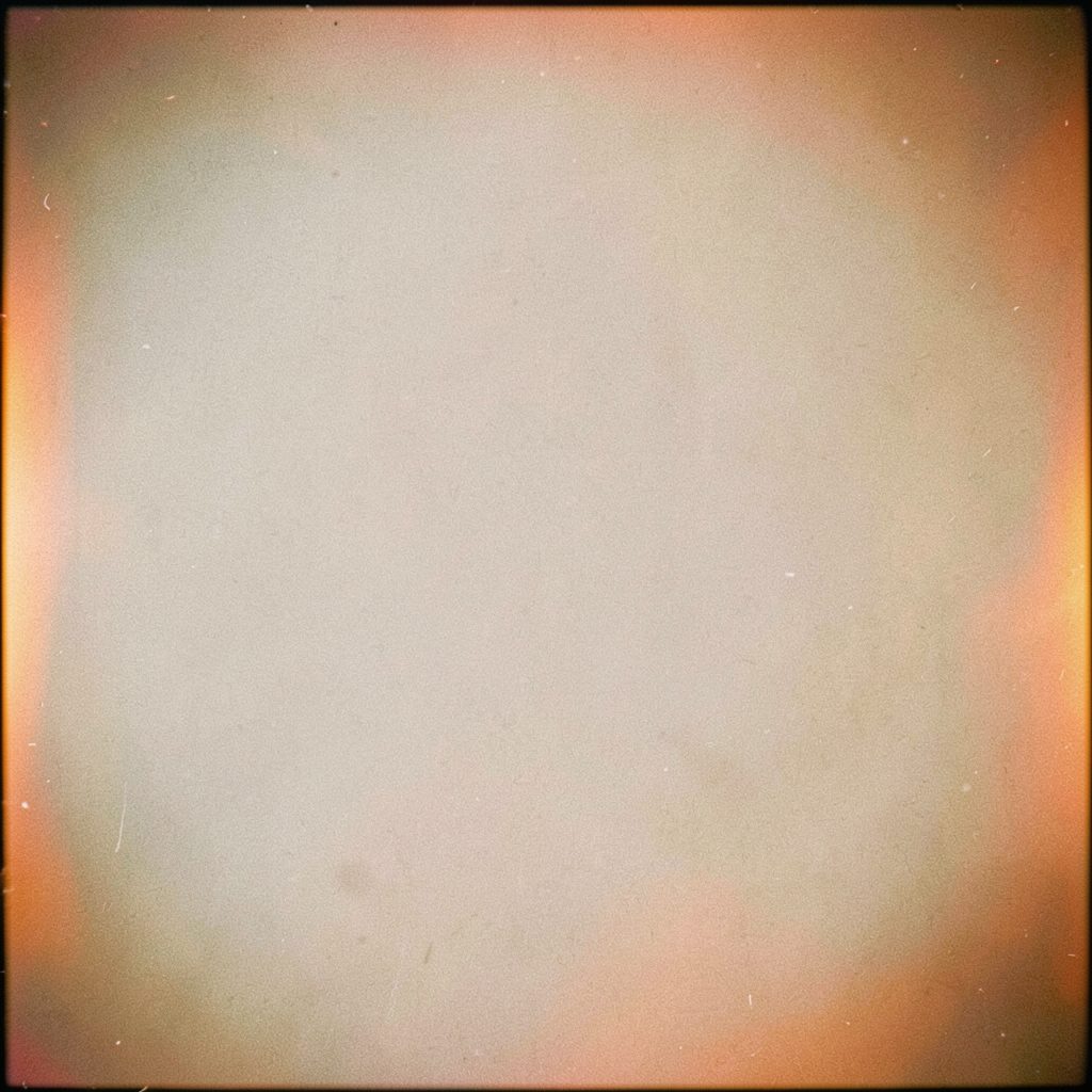 Small square grainy analog photograph of a simple outdoor scene in muted cream and brown tones